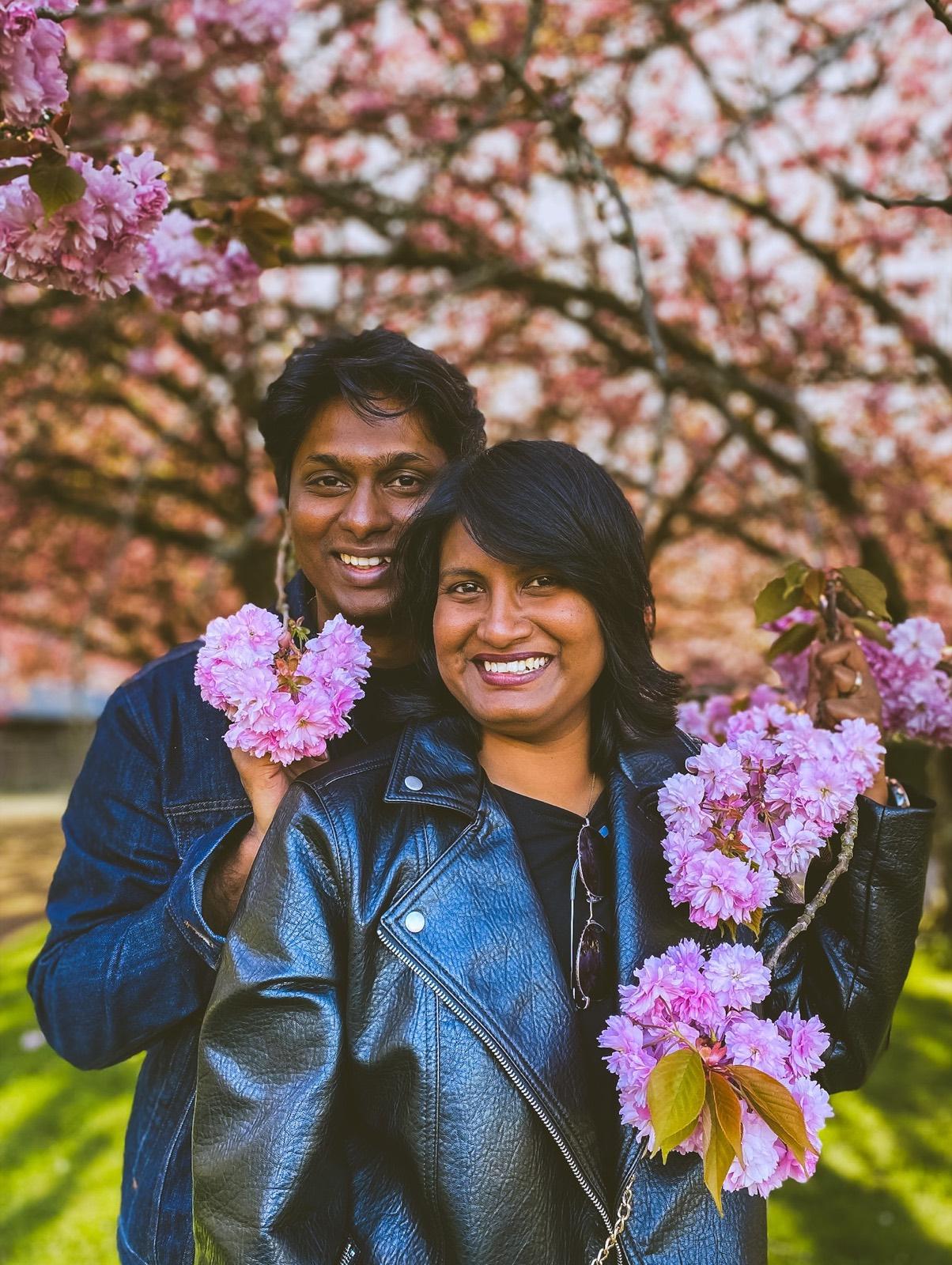 Fredrick and his wife smiling together beneath a cherry tree in full blossom.