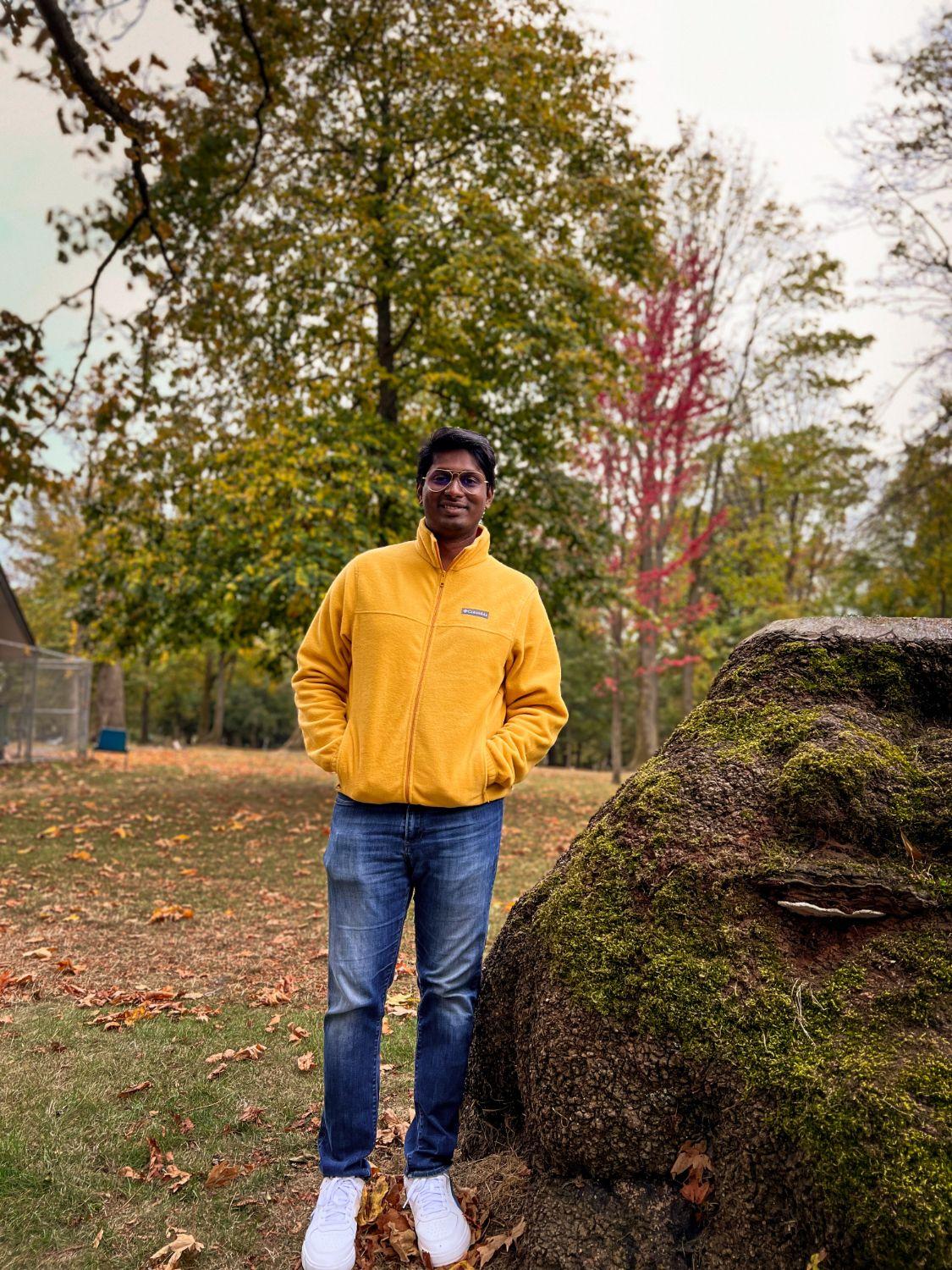 Fredrick in a yellow fleece jacket, standing in a park among autumn trees.